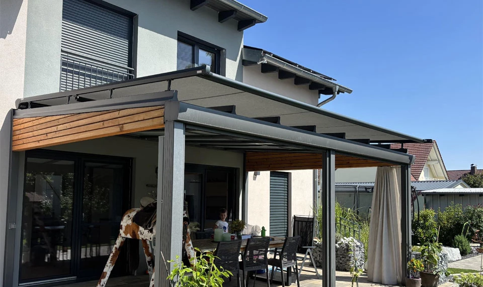 Moderne Wintergartenmarkise Moderne Wintergartenmarkise mit grauem Gestell und Holzverkleidung an einem Einfamilienhaus, bietet Sonnenschutz über der Terrasse mit Sitzbereich.